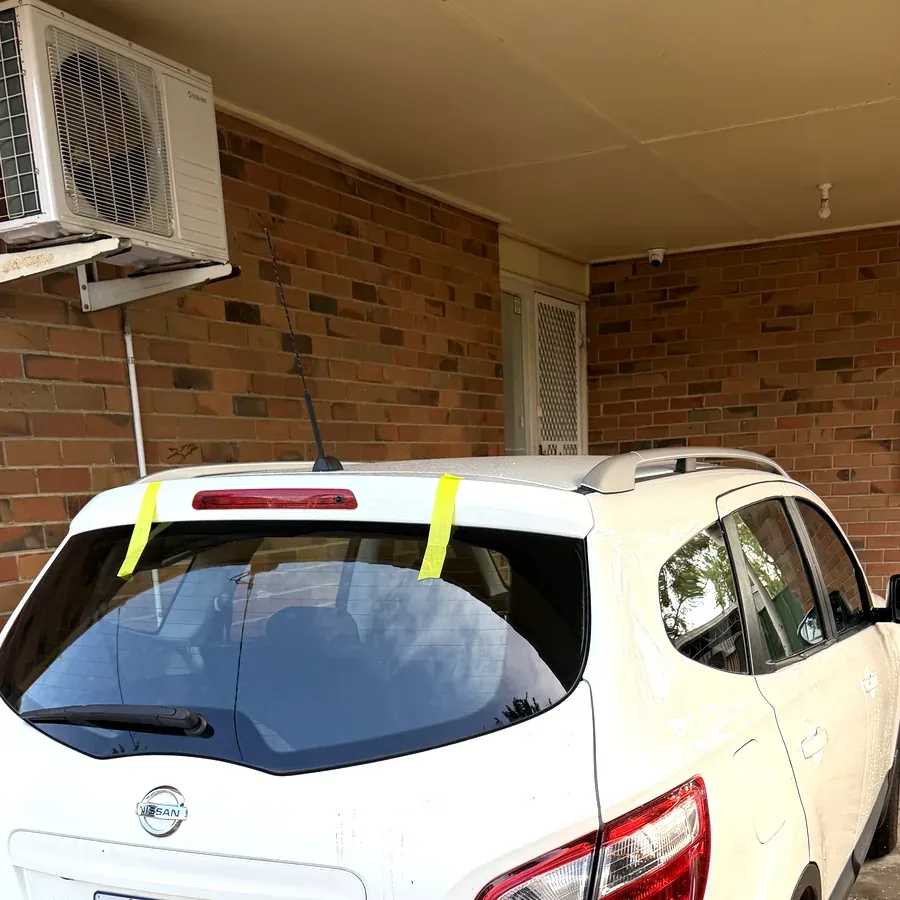 Replacement rear window fitted to a white hatchback under a home carport