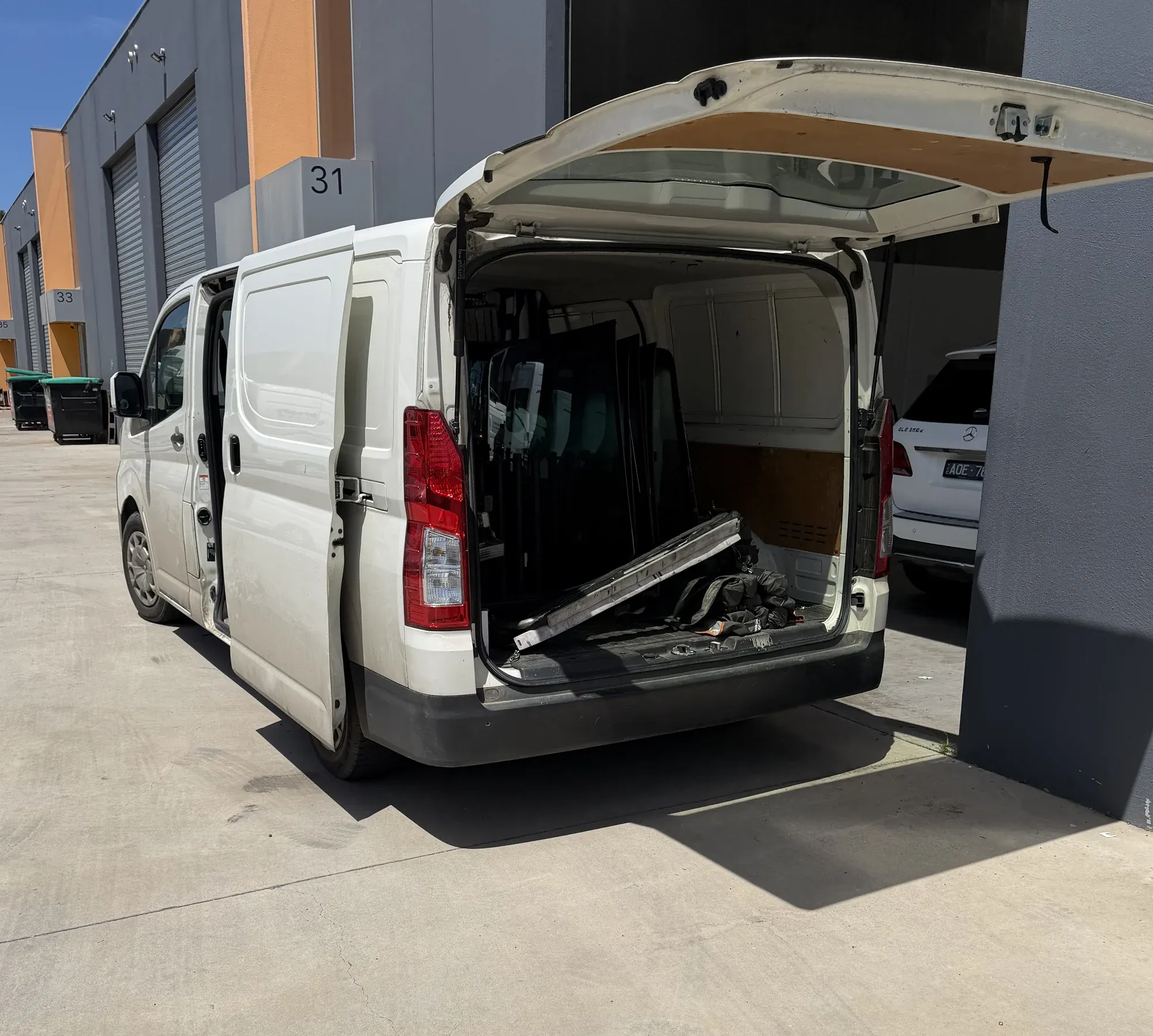 Mobile auto glass service van with rear doors open and glass racks visible, set up for an on-site job