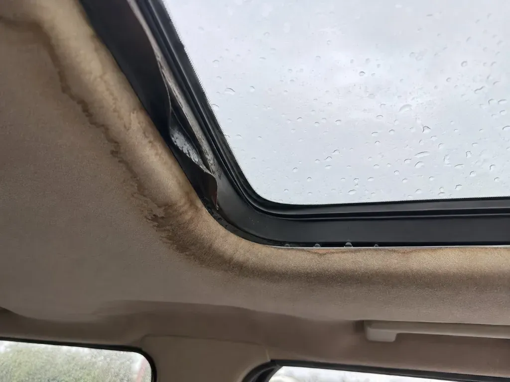 Before: interior view of a sunroof with a damaged seal and water staining on the headlining